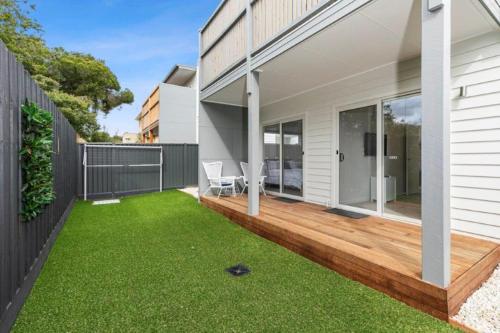 a backyard with a wooden deck and green grass at CASA EMEC- luxury, aircon, walk to the shops and beach! Outdoor shower and garage parking in Ocean Grove