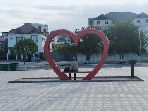 a person sitting on a bench with a heart sculpture at Seaside apartment in Aktau