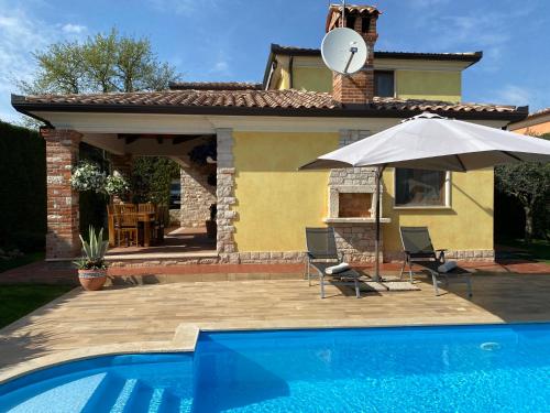 a pool with two chairs and an umbrella next to a house at Villa Eva Karigador in Novigrad Istria
