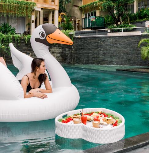 a woman sitting on an inflatable swan in a pool at Graha Socio Hotel Nusa Dua Bali in Nusa Dua