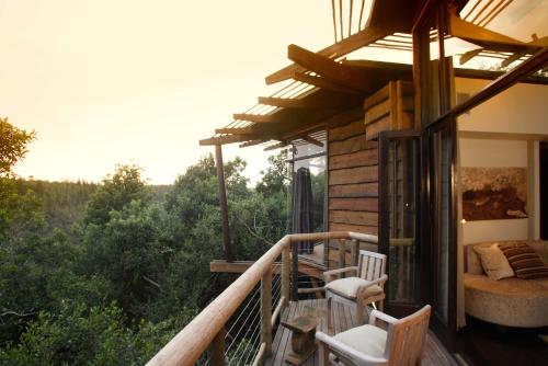 a balcony of a house with a bed and chairs at Tsala Treetop Lodge in Plettenberg Bay