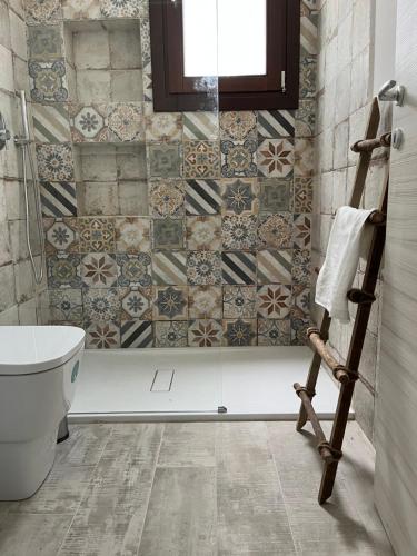 a bathroom with a toilet and tiles on the wall at MANZIL Country House in Valderice