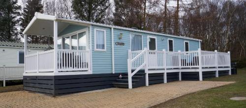 una casita azul con porche y barandilla blanca en Silver Birch Retreat - Percy Woods Country Retreat With 18 HOLE FREE GOLF, en Alnwick