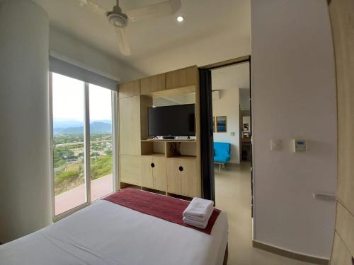 a bedroom with a bed and a tv and a window at Terrazas Tayrona Travelers Apartamentos y Suites in Santa Marta