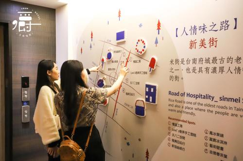 two women standing in front of a wall with a poster at Roots Chew Hotel in Tainan