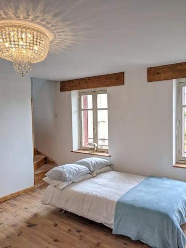 a bedroom with a bed with a chandelier and two windows at Trois Mousquetaires Gîte in Saint-Dizier-Leyrenne