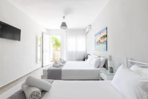 a white bedroom with two beds and a tv at Valasi Studios in Skála Foúrkas