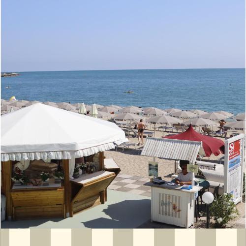 a beach with umbrellas and a person sitting at a desk at Maison Del Conero - Ombrellone e Lettini in Spiaggia Inclusi in Numana