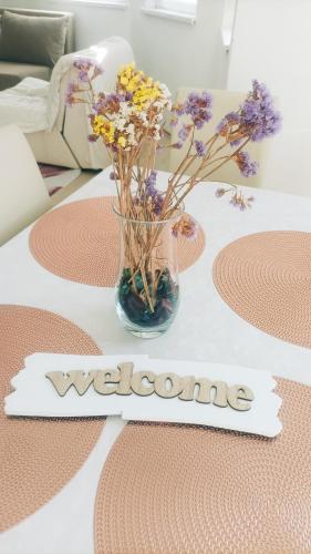 a vase of flowers on a table with a welcome sign at Dina apartman Jablaničko jezero in Konjic
