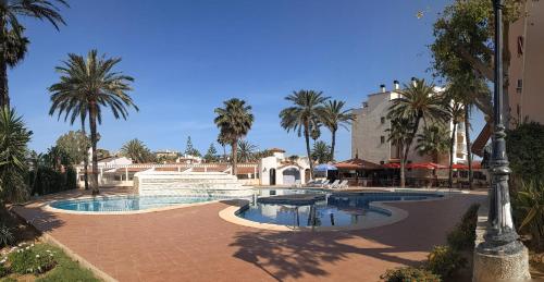 a swimming pool with palm trees and a building at Estudio con Piscina, Playa y Wifi in Denia