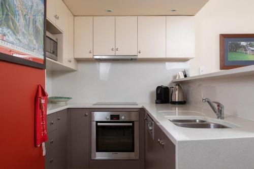 a small kitchen with white cabinets and a sink at Squatters Run 12a in Thredbo