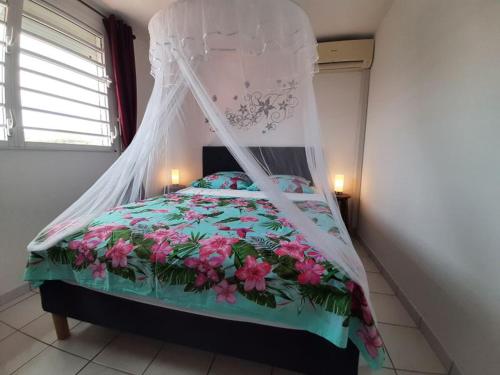 een slaapkamer met een hemelbed met roze bloemen bij Appartement le Marin avec vue sur mer in Le Marin