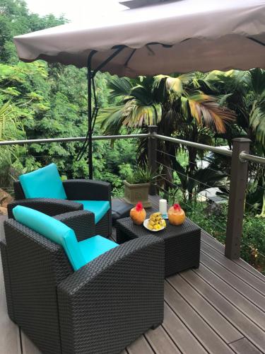 a deck with chairs and a table and an umbrella at Rock and Palm Lodge Self catering appartment in Baie Lazare Mahé