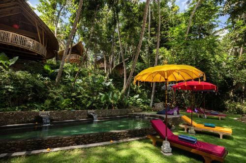 a pool with two umbrellas and chairs in a yard at Bamboo Turtles Ecolodge in Ubud