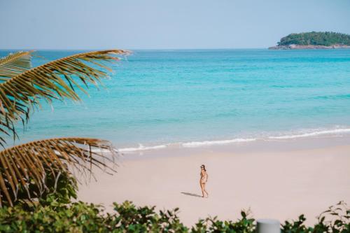 a woman walking on a beach near the ocean at The Shore At Katathani - Adult Only - SHA Extra Plus in Kata Beach