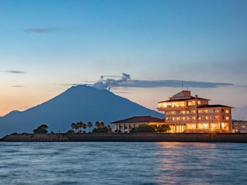 a large building with a mountain in the background at LiVEMAX RESORT Sakurajima Sea Front in Tarumizu