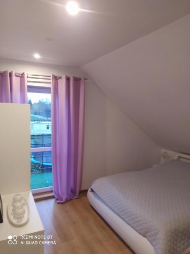 a bedroom with a bed and a window with purple curtains at Apartament u Małgosi in Kołczewo