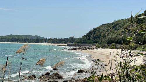 a beach with the ocean and rocks and trees at PHOENIX MINH CHÂU HOTEL in Quang Ninh