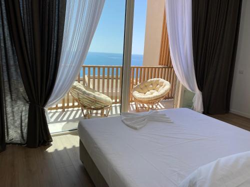 a bedroom with a bed and two chairs on a balcony at Green Coast 136 in Dhërmi