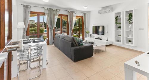 uma sala de estar com um sofá, uma mesa e uma televisão em Pool side ground floor apartment BF02 - Theseus Village, Aphrodite Hills Resort em Kouklia