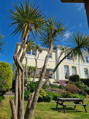 a picnic table in front of a house with palm trees at Meadowside Holiday Apartments in Torquay