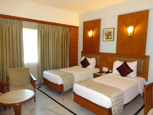 a hotel room with two beds and a chair at JP Chennai Hotel in Chennai