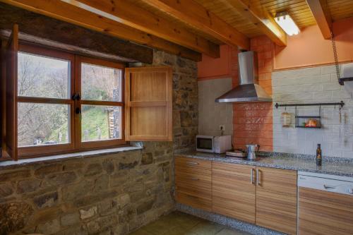 una cocina con armarios de madera y una pared de piedra. en Llananzanes Rural, en Llananzanes