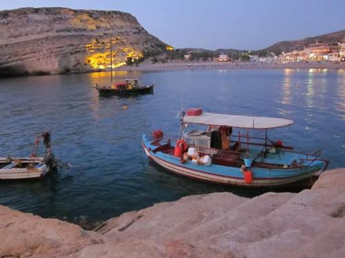 a small boat in the water near a rocky shore at Tsaner Apartment and Rooms in Matala