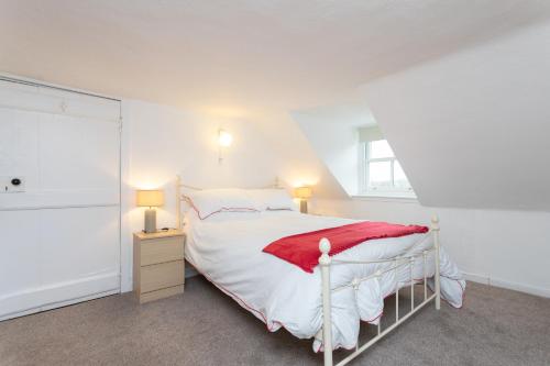 a white bedroom with a bed with a red blanket at The Auld Sweetie Shop in Perth