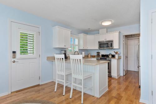 a kitchen with white cabinets and a island with chairs at The Emerald Owl House - Peaceful Emerald Isle Beach House w/ Luxurious Heated Pool! in Emerald Isle