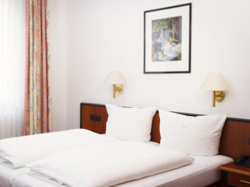 ein Schlafzimmer mit einem Bett mit weißer Bettwäsche und zwei Lampen in der Unterkunft Hotel Brößler in Stockstadt am Main