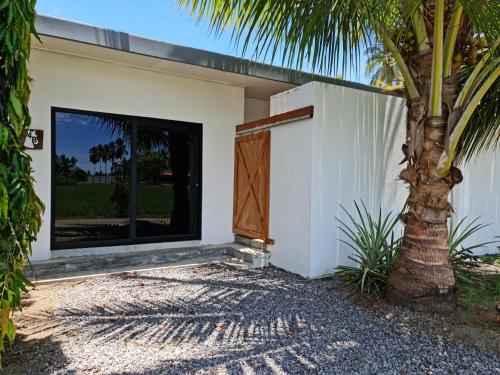 a white house with a door and a palm tree at Show Pony Beach Resort and Suites in Las Lajas