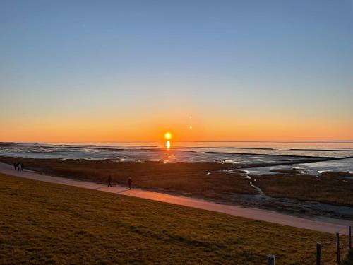 a sunset over the ocean with people walking on the beach at Ankertau in Norden
