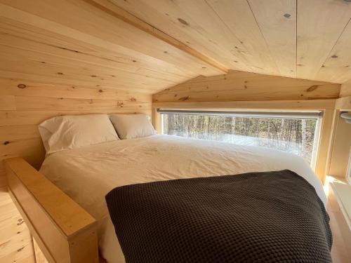 a bed in a tiny house with a window at Trailside Stays in Rumney