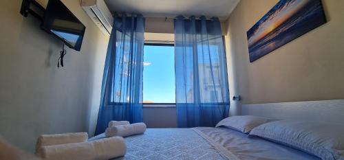 a bedroom with a bed and a window with blue curtains at B&B Aria di Mare - Pollina Sicilia in Finale
