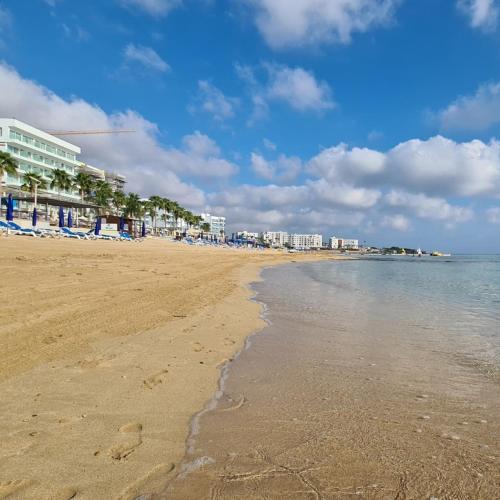 a beach with chairs and buildings and the ocean at Vrissiana Boutique Beach Hotel in Protaras