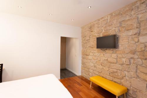 1 dormitorio con pared de piedra, cama y banco amarillo en Hotel Mimosa Paris, en París