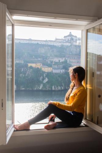 a woman sitting on a window sill looking out at Oporto Trendy River in Porto