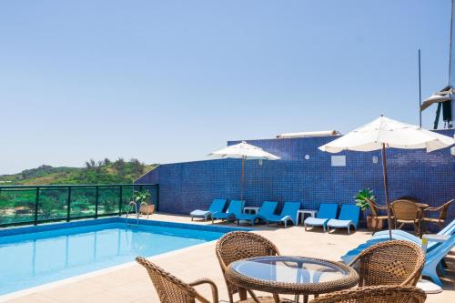 a swimming pool with chairs and a table and umbrella at Mediterrane Hotel by Castelo Itaipava in Arraial do Cabo