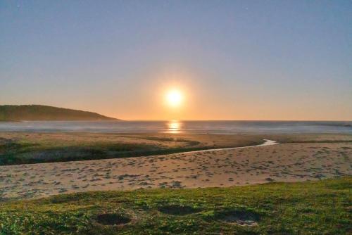 a beach with the sun rising over the ocean at Ingenia Holidays Merry Beach in Kioloa