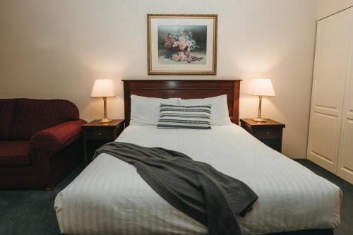 a bedroom with a bed and a chair and two lamps at The Lawson Riverside Suites in Wagga Wagga