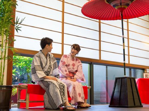 a man and woman sitting on chairs under a red umbrella at LiVEMAX RESORT Kaga Yamashiro in Kaga
