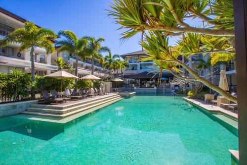a swimming pool with palm trees and buildings at Santai Sea-Duction in Casuarina