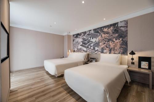 two beds in a hotel room with a painting on the wall at Atour Hotel Zhenjiang Xijindu Jinshan Temple in Zhenjiang