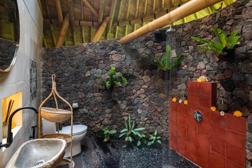 a bathroom with a toilet and a stone wall at Bamboo Turtles Ecolodge in Ubud