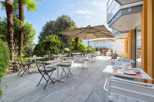 un patio con tavoli, sedie e ombrellone di Jazz Hotel Ascona ad Ascona