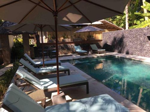 a swimming pool with umbrellas and lounge chairs next to it at Rumah Kelapa Sepi in Karangasem