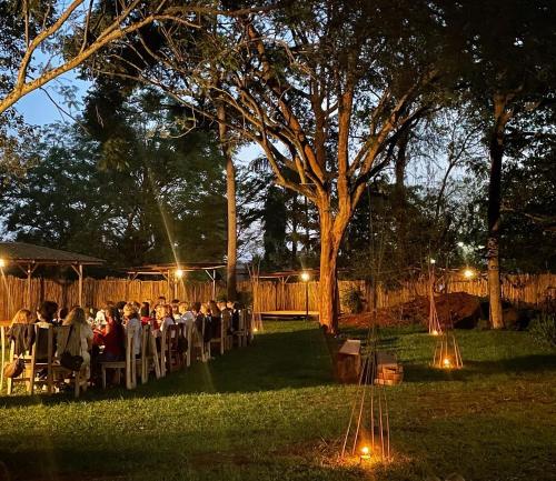 um grupo de pessoas sentadas a mesas num jardim à noite em Jinja Backpackers em Jinja