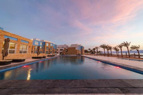 a large swimming pool with palm trees and buildings at Luxotel Aqaba Beach Resort & Spa Only 15 years plus in Aqaba