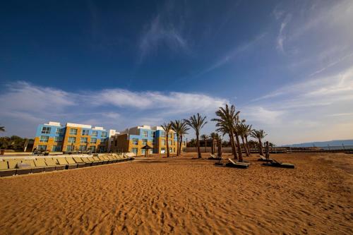 a sandy beach with palm trees and buildings on it at Luxotel Aqaba Beach Resort & Spa Only 15 years plus in Aqaba